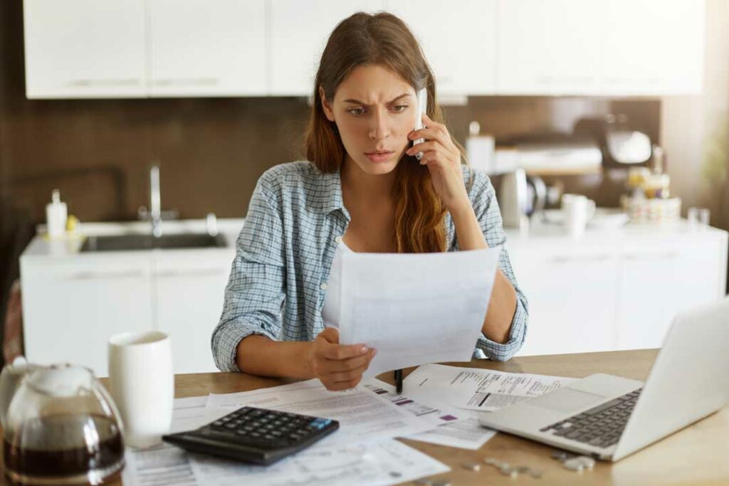 Woman reviewing bills, calculator in hand, looking concerned or tired